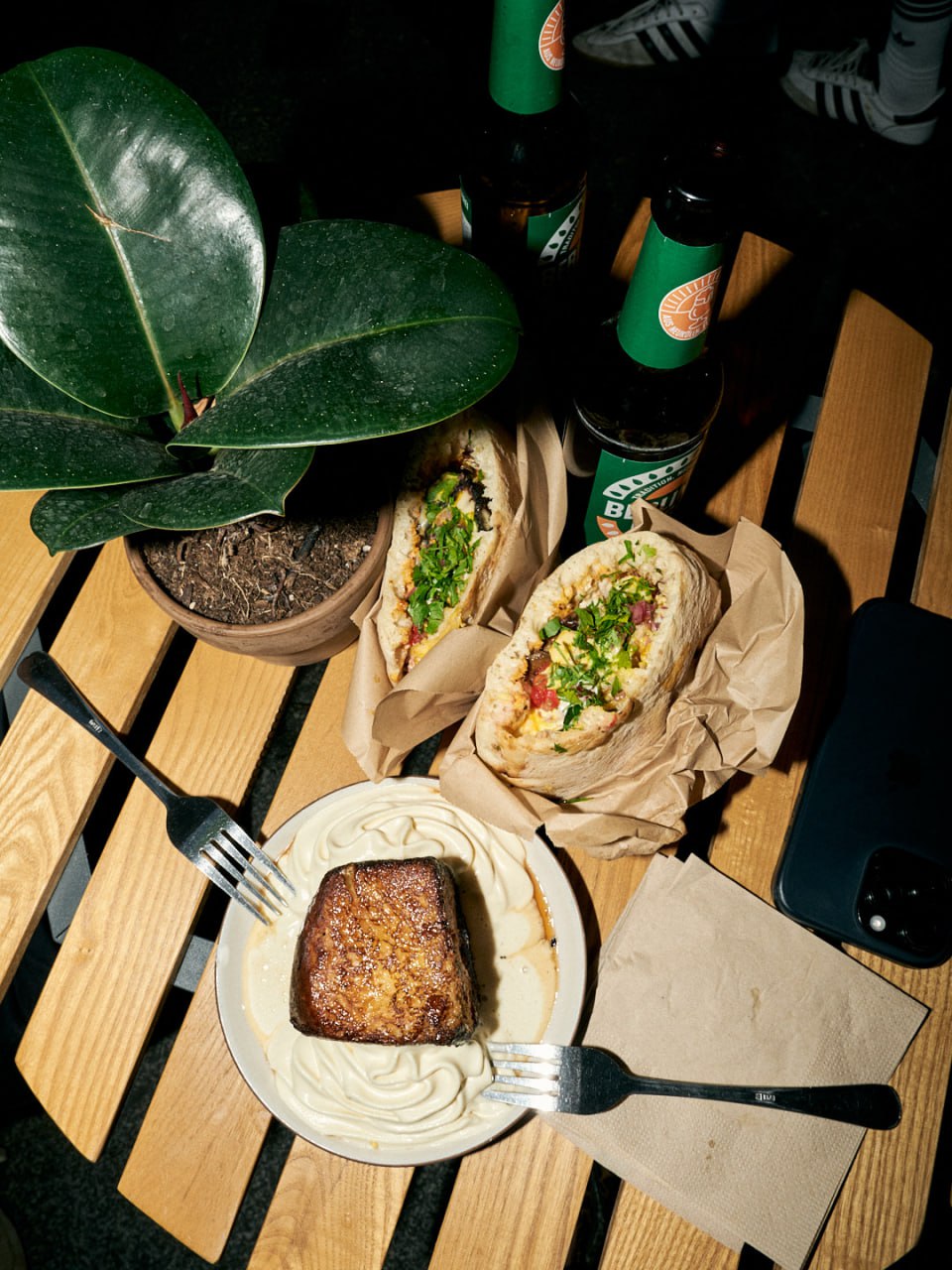 Overhead view of two sabich pitas, French toast with whipped cream, and Berliner Berg beers on a wooden table